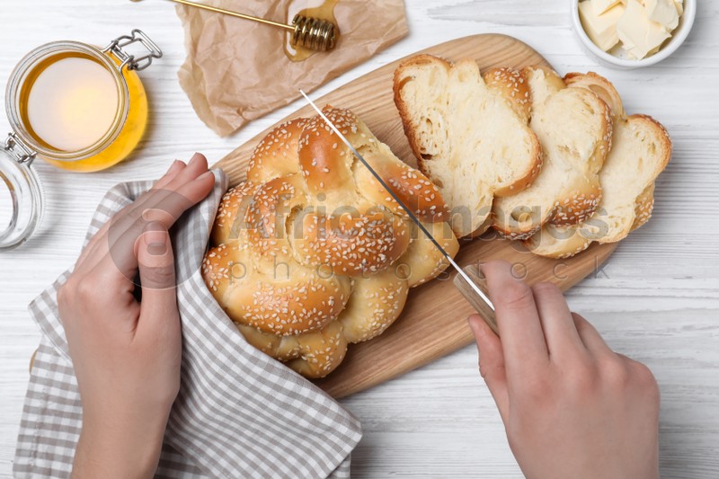 Photo of Woman cutting homemade braided bread at white wooden table, top view. Traditional Shabbat challah
