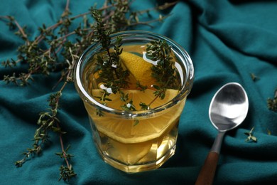 Photo of Glass of aromatic herbal tea with thyme and lemon on teal fabric