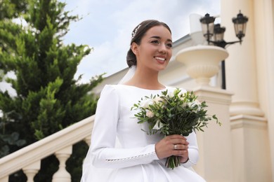 Young bride wearing wedding dress and engagement ring with beautiful bouquet outdoors