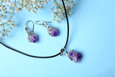 Beautiful silver necklace and pair of earrings with amethyst gemstones on light blue background