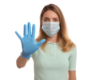 Young woman in medical gloves and protective face mask showing stop gesture against white background, focus on hand