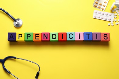 Photo of Word Appendicitis made of color cubes, stethoscope and pills on yellow background, flat lay
