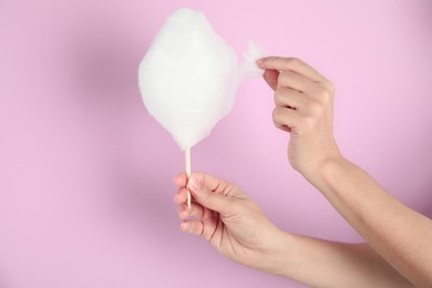 Woman eating yummy cotton candy on color background, closeup