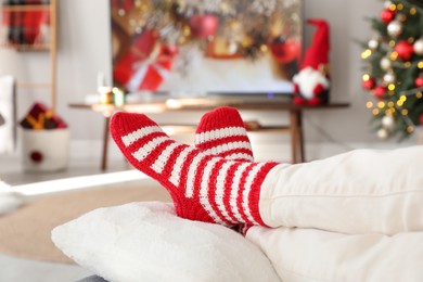 Woman in cute knitted socks watching TV at home, closeup