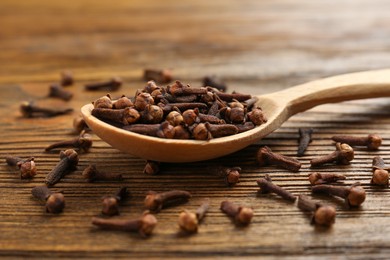 Aromatic dry cloves and spoon on wooden table, closeup