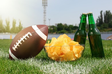 American football ball with beer and chips on green field grass in stadium
