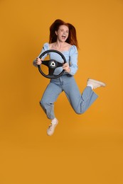 Excited young woman jumping with steering wheel on yellow background