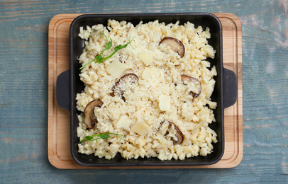 Photo of Delicious risotto with cheese and mushrooms on light blue wooden table, top view