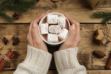 Woman with cup of delicious marshmallow cocoa at wooden table, top view