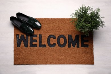 New clean mat with word WELCOME, shoes and plant on floor, top view