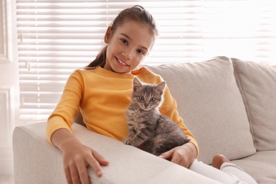 Cute little girl with kitten on sofa at home. Childhood pet