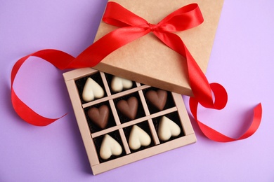 Tasty heart shaped chocolate candies on violet background, flat lay. Happy Valentine's day