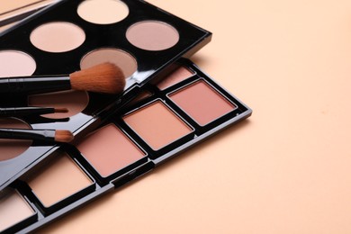 Photo of Colorful contouring palettes and brushes on beige background, closeup. Professional cosmetic product