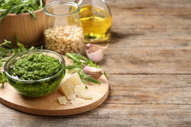 Bowl of tasty arugula pesto and ingredients on wooden table. Space for text