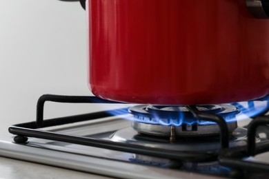 Red pot on stylish kitchen stove with burning gas, closeup
