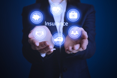Businesswoman holding different icons on dark blue background, closeup. Insurance concept