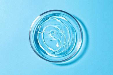 Petri dish with liquid on light blue background, top view