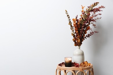 Vase with branches and candle on table near white wall, space for text