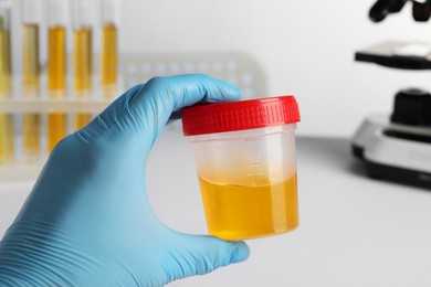 Photo of Nurse holding container with urine sample for analysis in laboratory, closeup