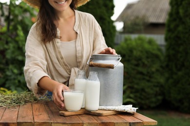 Photo of Smiling woman taking glass with fresh milk at wooden table outdoors, closeup