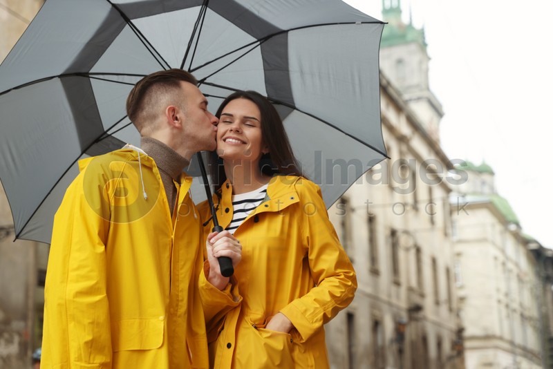 Lovely young couple with umbrella kissing under rain on city street