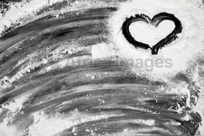 Drawing of heart on flour scattered over black table, top view