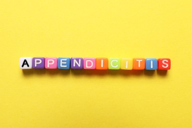 Word Appendicitis made of color cubes with letters on yellow background, top view