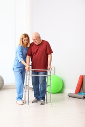 Caretaker helping elderly man with walking frame indoors