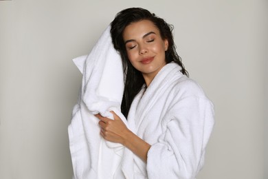 Beautiful young woman in bathrobe drying hair with towel on light background