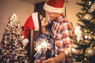 Couple holding sparklers in room decorated for Christmas