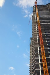Construction site with tower crane near unfinished building under cloudy sky, low angle view