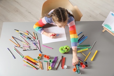 Little girl painting picture at table with painting tools indoors, top view