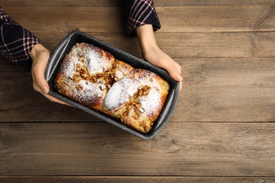 Photo of Woman holding baking pan with delicious yeast dough cake at wooden table, top view