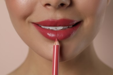 Young woman applying beautiful pink lip pencil on light background, closeup