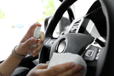 Woman cleaning steering wheel with wet wipe and antibacterial spray in car, closeup