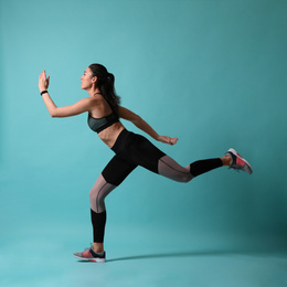 Athletic young woman running on turquoise background, side view