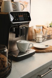 Modern coffee machine with cup of cappuccino in kitchen