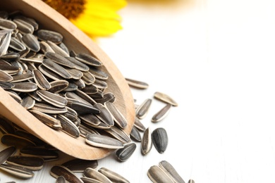 Raw sunflower seeds and scoop on white wooden table, closeup. Space for text