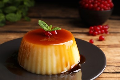 Photo of Plate of delicious caramel pudding with red currants and mint on wooden table, closeup
