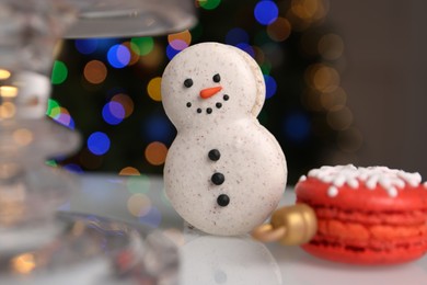 Beautifully decorated Christmas macarons on white stand against blurred festive lights, closeup