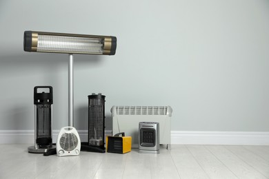 Different electric heaters near light grey wall indoors. Space for text