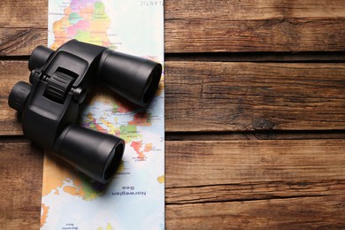 Modern binoculars and map on wooden table, top view. Space for text