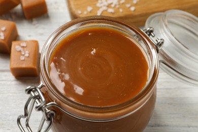 Yummy salted caramel in glass jar on white table, closeup