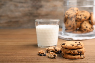 Tasty cookies with chocolate chips and glass of milk on wooden table