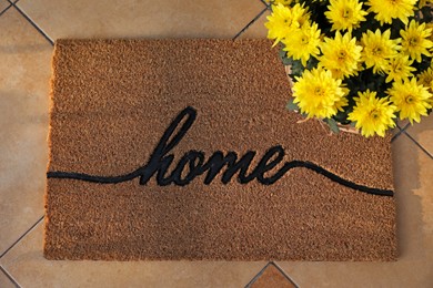 Photo of Doormat with word Home and flowers on tiled floor, flat lay