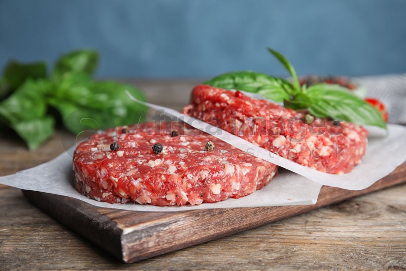 Raw meat cutlets for burger on wooden table against blue background, closeup