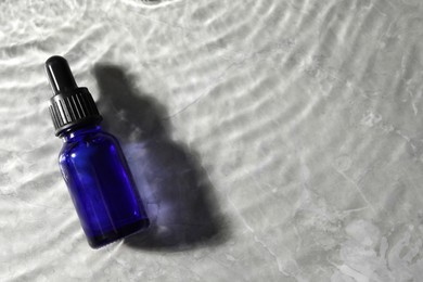 Bottle of face serum in water on light background, top view. Space for text