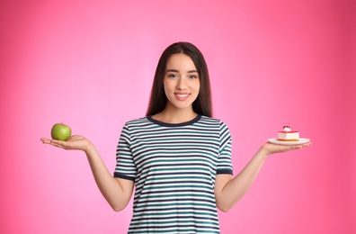 Concept of choice. Woman holding apple and cake on pink background