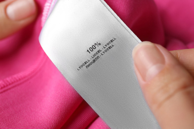 Woman reading clothing label with material content on pink shirt, closeup