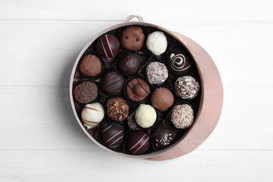 Box with tasty chocolate candies on white wooden table, flat lay